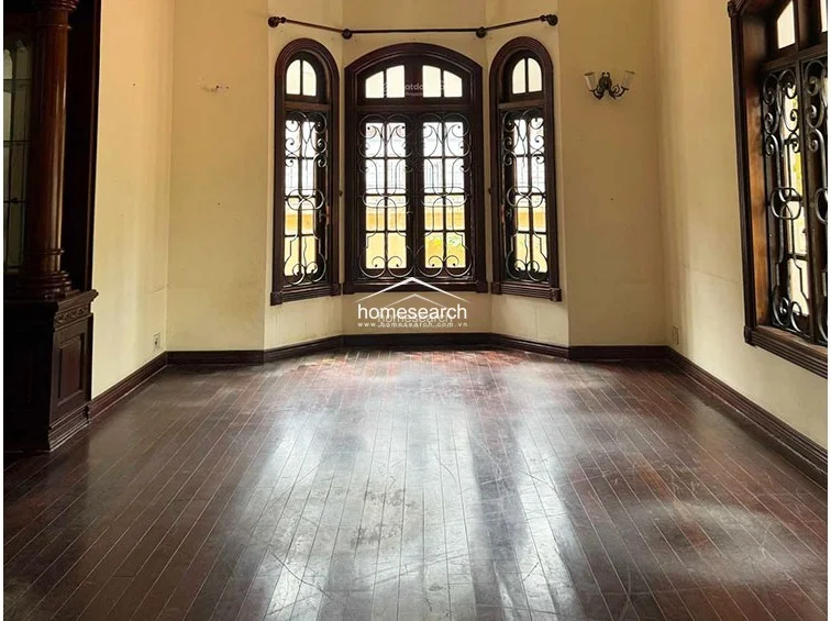 This room features a classic bay window design with arched frames and decorative ironwork, providing a focal point that invites ample natural light. The interior is characterized by warm, neutral walls, dark wood trim, and polished hardwood floors, maintaining a consistent and elegant aesthetic throughout the home.