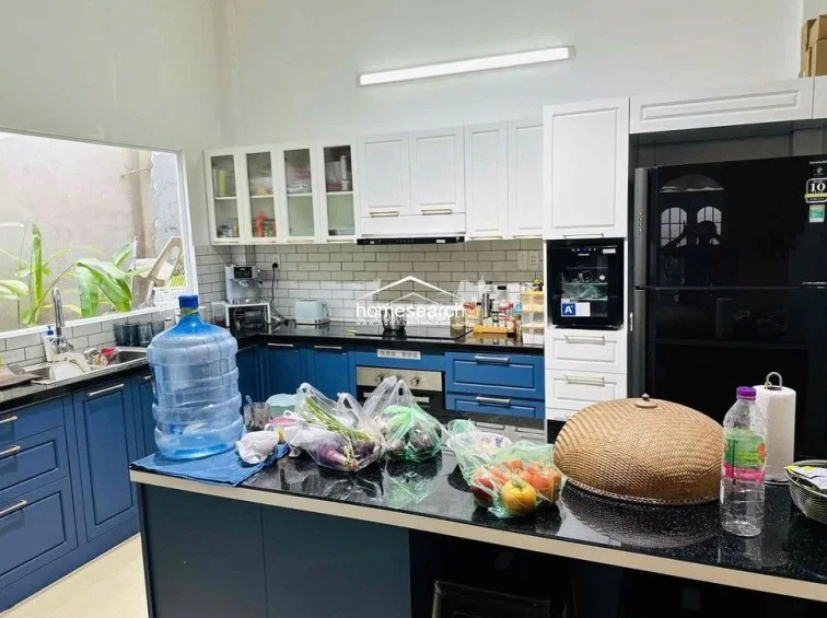 This modern kitchen is well-equipped with a contrasting color scheme of deep blue lower cabinets and crisp white upper cabinetry, paired with a sleek black countertop. A large window provides natural light and a view of the greenery outside, while the subway tile backsplash and integrated appliances suggest a functional, well-maintained cooking space.