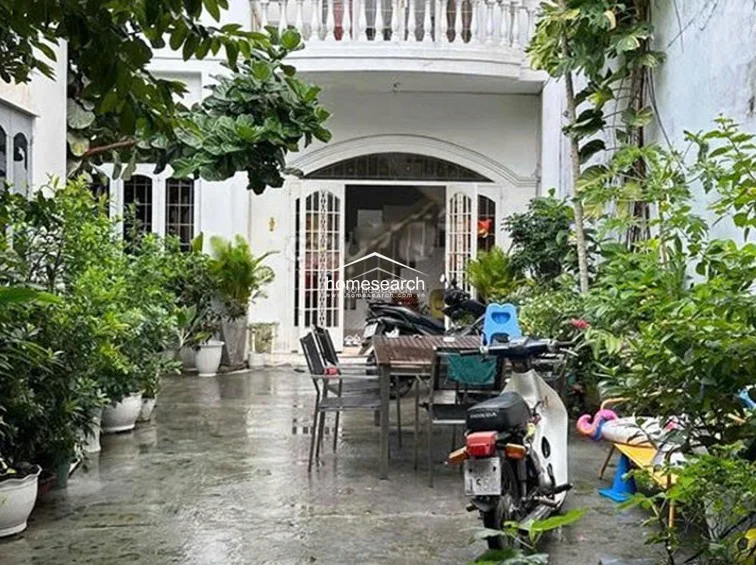 This outdoor courtyard serves as a functional transition space, featuring a concrete patio area furnished with a dining table and chairs. The area is lush with potted greenery, providing a natural buffer, and connects directly to the home's interior through elegant arched glass-paneled doors.