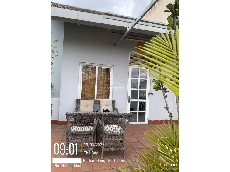 Featuring a similar layout to the previous terrace view, this angle highlights the exterior wall finish and the integration of the outdoor furniture. The area is partially shaded by an overhead structure and benefits from a tranquil garden setting, contributing to the property's overall well-maintained appearance.