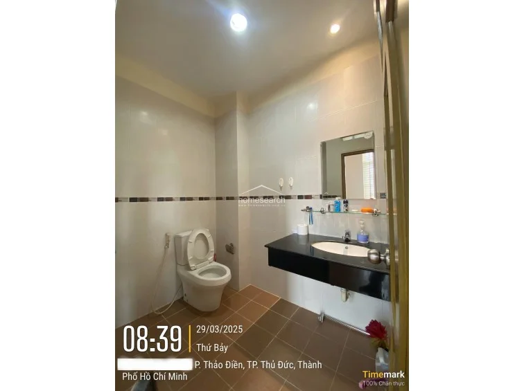 This view of the bathroom highlights the efficient layout, featuring a standard white toilet with a bidet sprayer and a floating vanity design that maximizes floor space. The room maintains a consistent design language with the previous image, utilizing earthy floor tiles and recessed ceiling lighting to create a bright, clean environment.