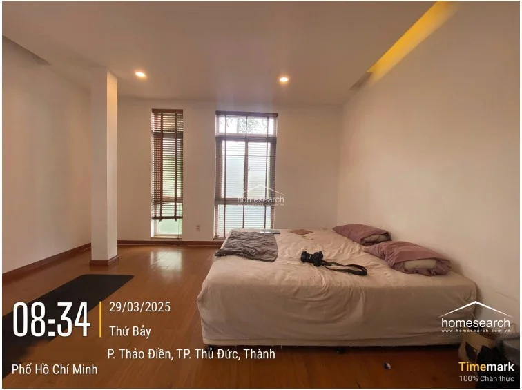 This image presents the same bedroom as the previous view, highlighting the clean, uncluttered layout and the ample floor space available. The room maintains a consistent design theme with white walls, wooden flooring, and wooden blinds that offer privacy while allowing for adjustable natural light. The condition of the room is excellent, emphasizing a minimalist approach to living.