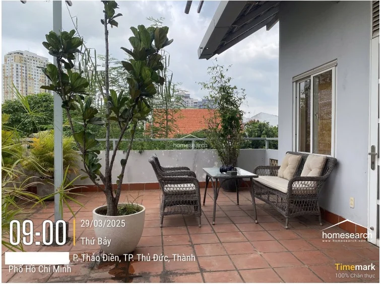 This outdoor terrace provides a serene, elevated seating area furnished with wicker-style chairs and a table, perfect for relaxation. The space is finished with terracotta-style floor tiles and is surrounded by lush greenery, offering a private and peaceful atmosphere.
