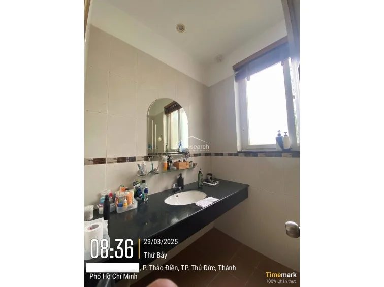 This bathroom is finished with neutral wall tiles accented by a decorative mosaic border and features a dark granite countertop with an integrated sink. A window provides natural light, and the space includes a simple arch-top mirror and glass shelving, reflecting a functional and well-maintained condition.