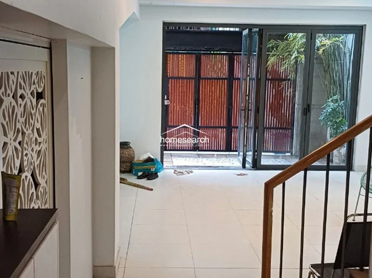 This open-plan living area is characterized by large, floor-to-ceiling glass folding doors that provide seamless access to the outdoor space and invite ample natural light. The interior features neutral white tile flooring and a modern, decorative white screen partition, creating a clean and airy flow throughout the ground level.