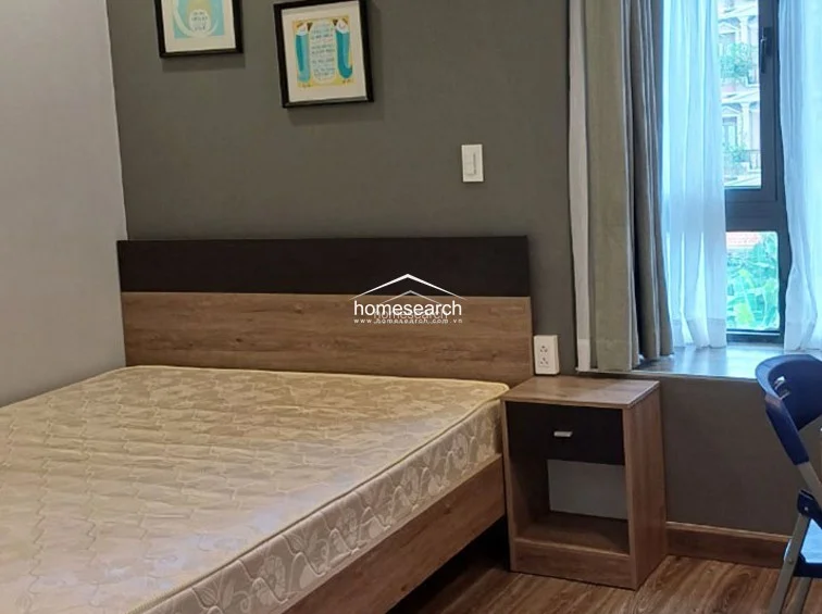 This bedroom is finished with a sophisticated grey accent wall and wood-look flooring, creating a modern and cozy aesthetic. It includes a matching wood-tone headboard and nightstand, with large windows that provide natural light and a view of the surrounding residential area.