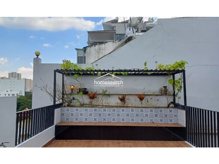 This outdoor terrace features a covered pergola structure adorned with climbing plants, providing a shaded and relaxing retreat. The space is finished with decorative patterned tiles and wood-look flooring, offering a well-maintained area for outdoor leisure.