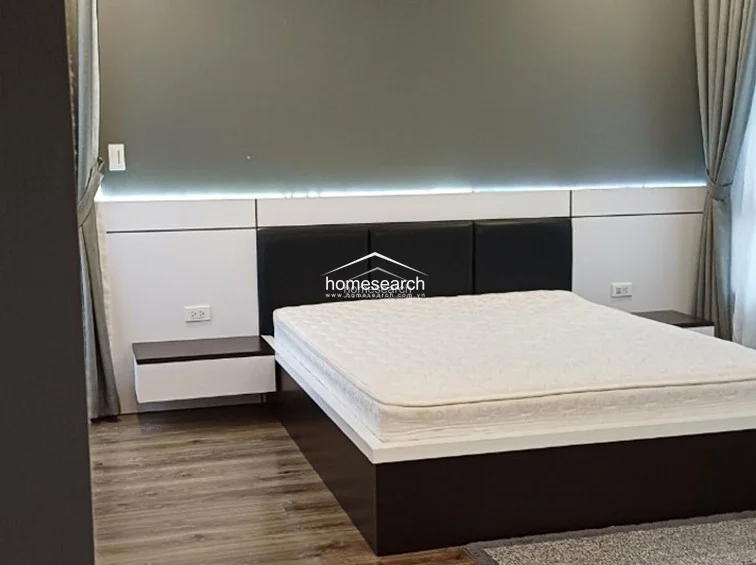 This view emphasizes the custom bed frame and headboard, which includes built-in floating nightstands and ambient strip lighting. The combination of dark leather upholstery, white panels, and wood-toned flooring creates a sophisticated and well-organized sleeping environment.