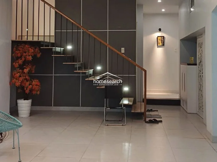 This area showcases a striking architectural staircase with a minimalist metal railing and wooden treads, set against a dark, grid-patterned feature wall. The space is well-lit with integrated stair lighting and a decorative potted plant, maintaining a contemporary and uncluttered aesthetic.