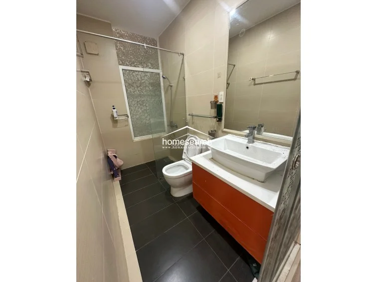 This contemporary bathroom is finished in neutral earth-toned wall tiles and dark floor tiles, creating a sophisticated contrast. It includes a floating vanity with an orange cabinet, a glass-enclosed shower area, and a large mirror that enhances the sense of space.