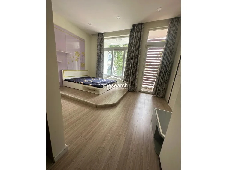 This bedroom is accented by a decorative purple wall panel with floral detailing behind a low-platform bed. The room includes a dedicated glass-paned door leading to an outdoor balcony and features modern recessed lighting throughout the ceiling.