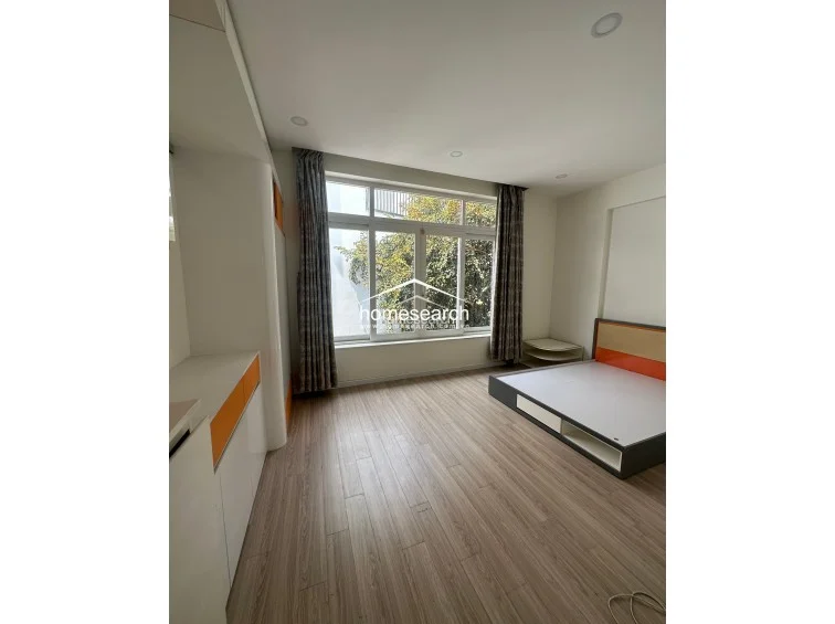 This bedroom highlights a modern, minimalist design with a low-profile bed frame featuring orange accent panels. The room is finished with light wood-look flooring and includes a built-in storage cabinet, maintaining a bright and airy atmosphere.