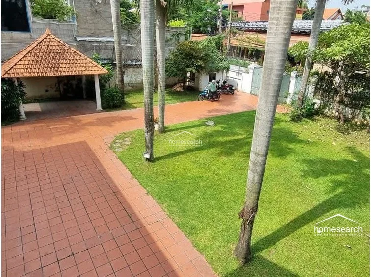 This elevated view provides a clear look at the property's layout, including the terracotta-tiled driveway, the covered pavilion, and the transition between the paved areas and the lawn. The site appears well-organized and secure, with clear pathways for vehicle access and ample space for outdoor activities.