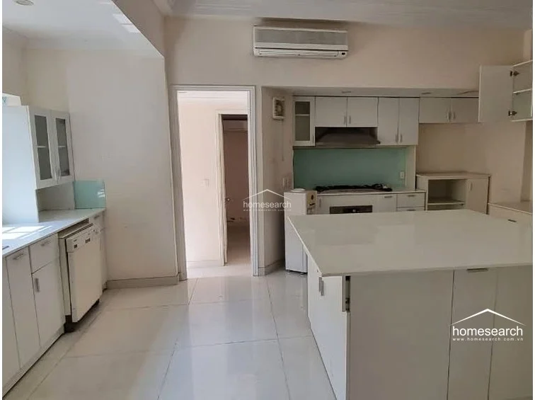 This kitchen features an open-concept layout with a central island and white cabinetry, providing a clean and functional workspace. The area is finished with light-colored tile flooring, a pale blue backsplash, and includes a wall-mounted AC unit for climate control. A doorway leads directly into an adjacent room, suggesting a seamless flow between the kitchen and the rest of the residence.