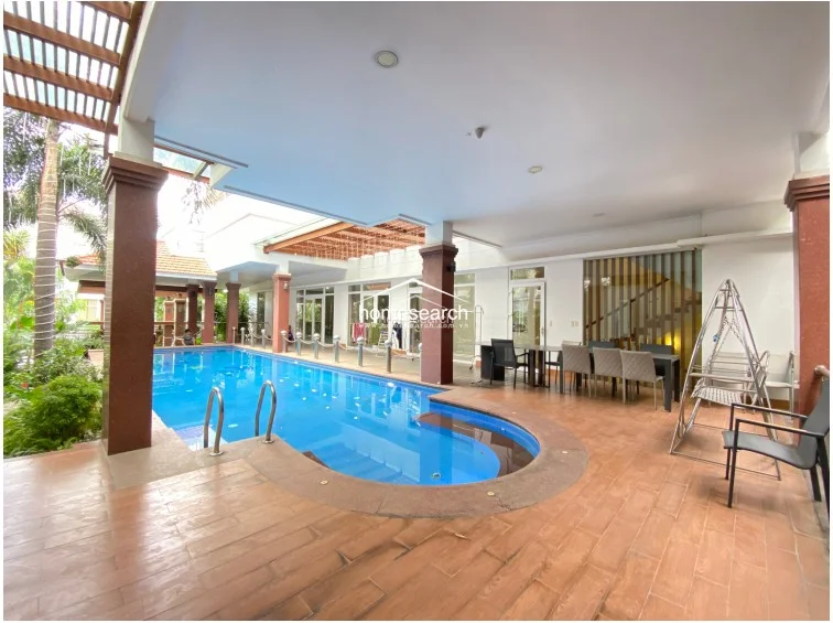 This expansive, open-concept living area flows directly onto the pool deck through large glass sliding doors, ensuring an abundance of natural light. The room is finished with polished light-colored tile flooring, neutral walls, and elegant floor-to-ceiling mauve curtains, while a modern ceiling fan and recessed lighting provide climate control and illumination.