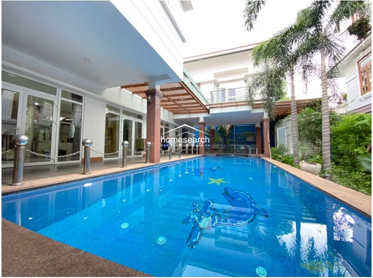 This view reveals a private swimming pool with a vibrant mosaic floor, situated directly adjacent to the main living area. The pool deck is finished with durable stone, and the surrounding architecture features large glass doors, allowing for seamless indoor-outdoor flow and abundant natural light.
