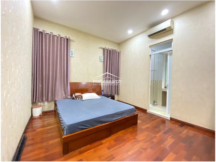 This bedroom view showcases a large, dark-wood built-in wardrobe that provides significant storage space, perfectly contrasting with the light, textured wall finishes. The room maintains a consistent design language with the rest of the home, featuring polished hardwood floors and recessed lighting. The layout is practical, with a clear flow toward the entrance and adjacent living spaces.