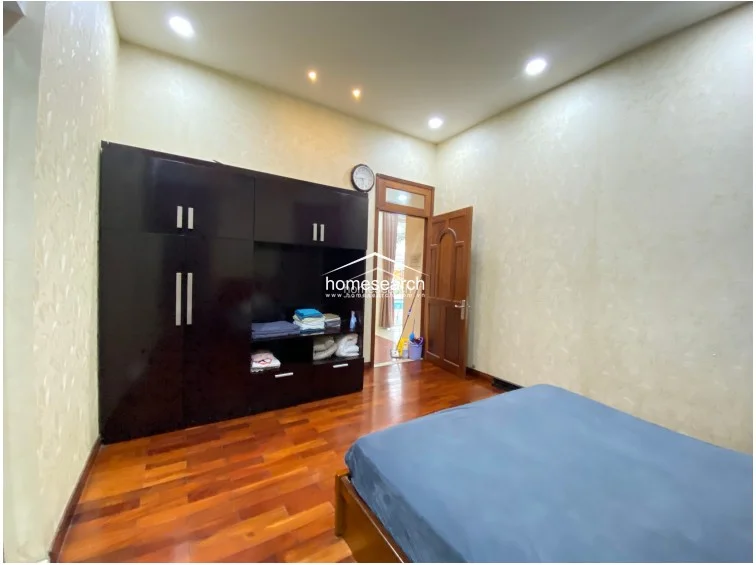 This bathroom features a functional layout with a glass-enclosed shower area separated from the vanity space by a partition. It is finished with two-toned wall tiles, a marble-topped vanity with an integrated sink, and a large wall-mounted mirror, though there are visible signs of wear and moisture damage near the mirror frame.