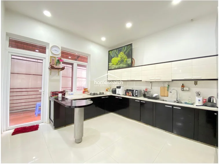 This kitchen view highlights the extensive storage capacity provided by the floor-to-ceiling black cabinetry and the sleek, modern aesthetic of the black and white color scheme. The layout includes a dedicated breakfast bar, glossy white tile flooring, and a large window that keeps the workspace bright and inviting. The overall condition appears excellent, with a clean, organized, and contemporary design.